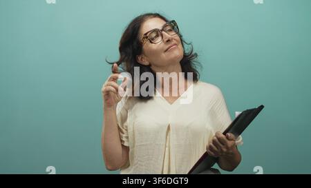 Woman holding clipboard and touching hair with glasses, hand to head gesture in studio; serenity confidence ease. Stock Photo