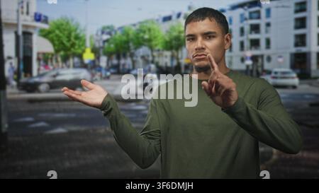 Man presenting open hand and pointing finger at invisible object in a busy city street intersection with cars and buildings; assertive instruction. Stock Photo