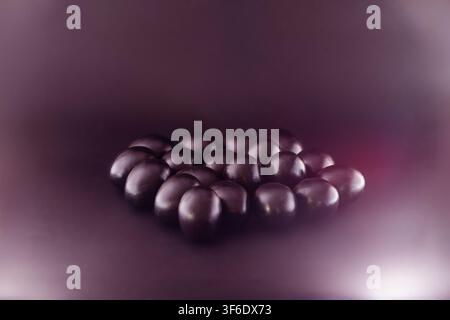Studio horizontal still life of many black painted eggs carefully arranged in a heart shape on a purple gradient background. The contrast between the Stock Photo