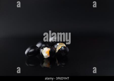 Wider horizontal studio still life of a group of black painted eggs with one cracked egg revealing its yolk, reflected on a dark glossy surface. The w Stock Photo