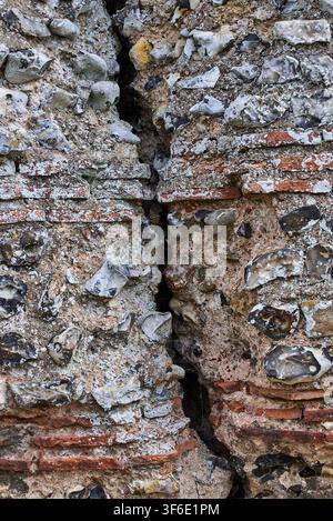A deep vertical structural crack splitting through layers of Roman flint masonry and bonding tiles at Burgh Castle fort in Norfolk, England. Stock Photo