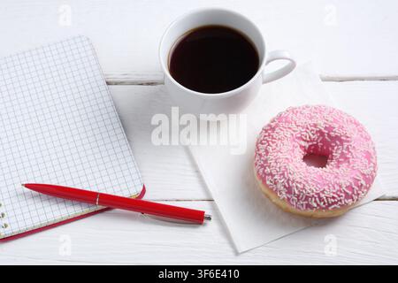 Notebook and pink donut with coffee on white wooden table Stock Photo