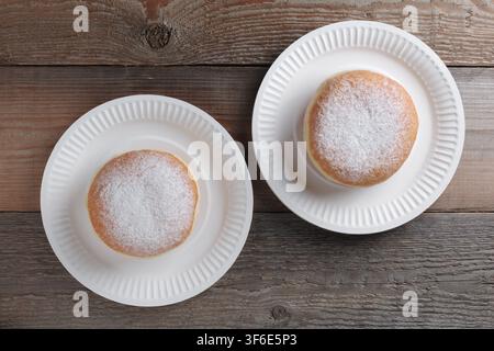 Two fresh donuts on a disposable plate on old wooden table, top view Stock Photo