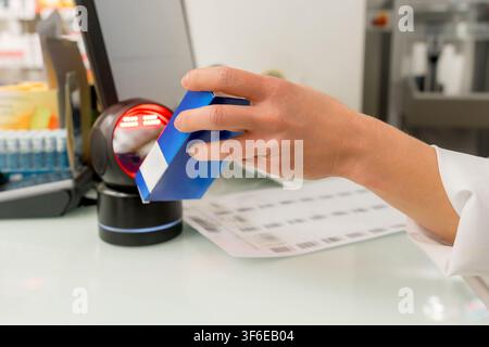Close-up of a pharmacist scanning a blue medicine package with a barcode reader at a pharmacy counter, illustrating prescription dispensing, healthcar Stock Photo