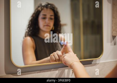 Woman touches a smart mirror display in a modern apartment bathroom, using connected home technology for a convenient, interactive daily routine. Stock Photo