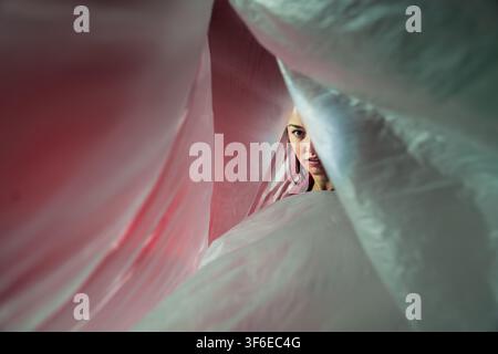 Latin woman dancer peers through flowing translucent fabric, creating an intimate abstract portrait with soft light, layered texture, and a dramatic c Stock Photo