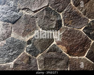 High-detail full-frame view of a decorative stone wall made from irregular natural slate and basalt tiles, showcasing warm earthy tones and rugged min Stock Photo