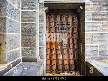 Old rusty metal folding security gate blocking an entrance doorway of an ancient grey stone building with textured blocks Stock Photo