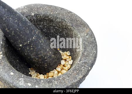 Rustic granite stone mortar and pestle crushing roasted peanuts on white background, showing traditional Asian kitchen tools for authentic cooking Stock Photo