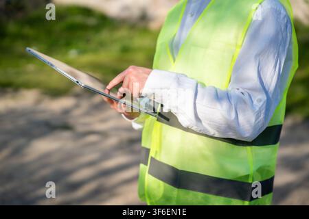 Engineer using tablet computer on construction site wearing safety vest. Digital workflow mobile construction documentation and engineering tools. Stock Photo