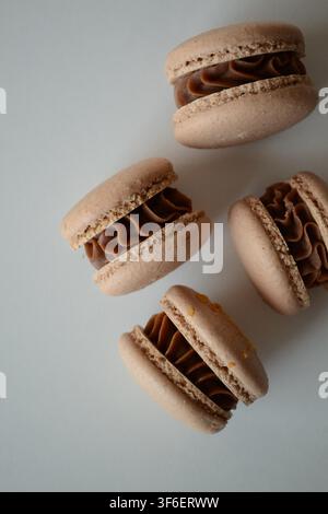 Four French peanut butter macarons with chocolate caramel ganache on white background, flat lay dessert composition Stock Photo