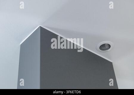 Abstract architectural detail featuring a sharp corner where a textured gray wall meets a white ceiling with a circular light fixture Stock Photo