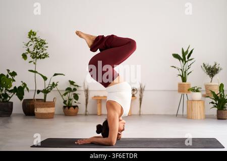 Young woman practicing supported headstand yoga pose at home studio Stock Photo