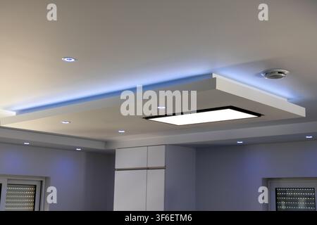 A contemporary ceiling features a multi-level design with integrated spotlights and a large illuminated panel, creating a sophisticated atmosphere Stock Photo
