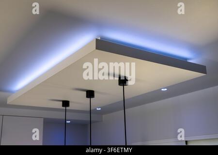 A contemporary interior features a suspended ceiling element with integrated blue LED strip lighting and three black pendant lights hanging below Stock Photo