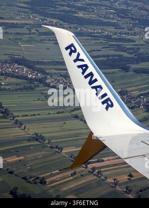 2026.06.25, Krakow, Poland: ryanair airplane wing flying over serene landscape with fields and towns below aerial view from the plane white blue green Stock Photo