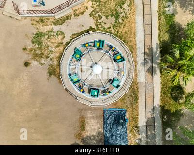 Aerial view of the circular carousel ride at Kashmir Park, featuring green seats and a central structure, surrounded by sandy grounds and palm trees i Stock Photo