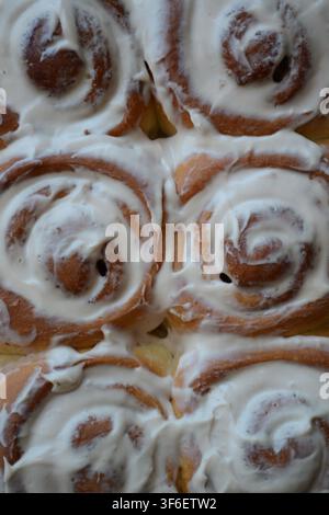 Freshly baked cinnamon rolls topped with cream cheese frosting close up, sweet homemade Cinnabon pastries top view Stock Photo
