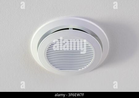 A close-up view of a circular white air vent installed in a textured ceiling, highlighting its minimalist design and functional purpose Stock Photo