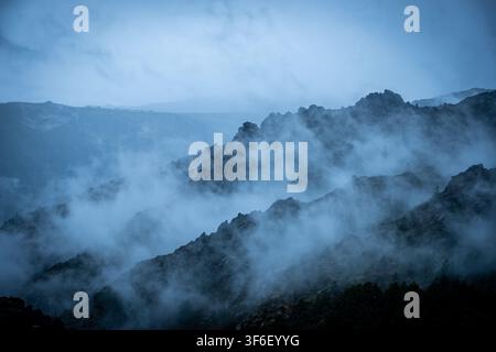 Rugged mountains shrouded in thick fog and low clouds during blue hour Stock Photo
