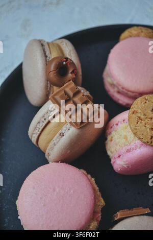 Assorted French macarons decorated with mini chocolate bars and cookies served on black plate Stock Photo