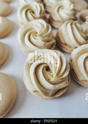 Process of piping vanilla buttercream swirls on macaron shell halves on parchment paper Stock Photo