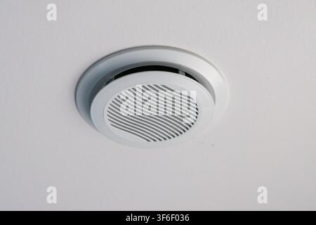 A circular white vent is installed on a textured white ceiling, providing air circulation and ventilation for the room Stock Photo