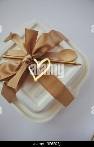 Eco friendly bento cake takeaway box decorated with satin ribbon golden candle wooden spoon and heart topper Stock Photo