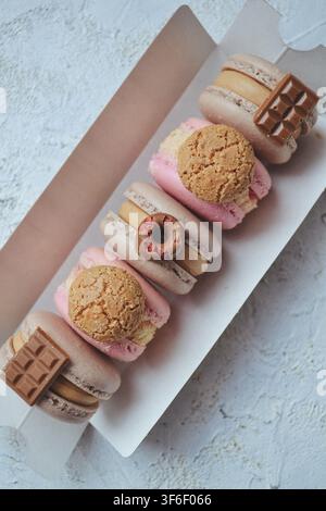 Assorted gourmet French macarons topped with mini chocolate bars and cookies in paper box Stock Photo
