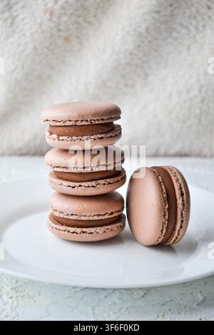 Stack of chocolate french macarons with ganache filling on white plate and light textured background Stock Photo