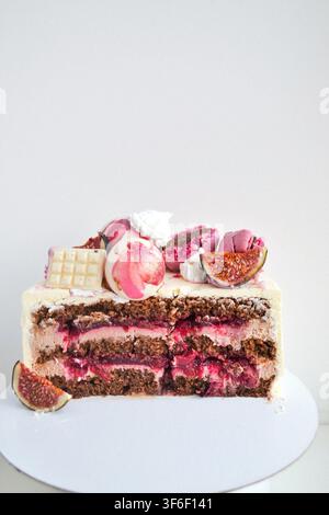 Half of chocolate layer cake with berry confit, decorated with fresh figs, macarons, and chocolates on white background Stock Photo