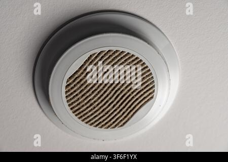 A dirty air vent on a white ceiling shows accumulated dust and grime on its filter, indicating a need for cleaning Stock Photo