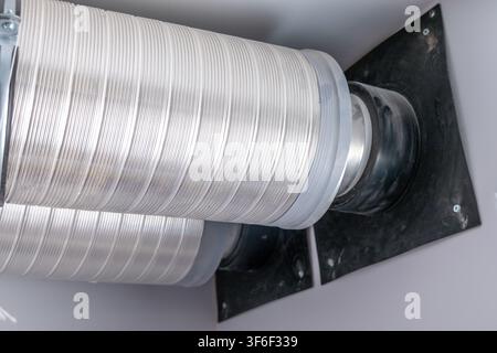 Close-up view of a silver flexible air duct system attached to a black mounting plate on a wall Stock Photo