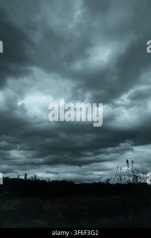 Dark storm clouds gather over a rural field and distant tree line, creating a dramatic, foreboding landscape before heavy rain Stock Photo
