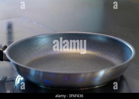 A close-up view of a clean, empty non-stick frying pan resting on a sleek induction cooktop, highlighting its metallic surface and the cooktop's indic Stock Photo