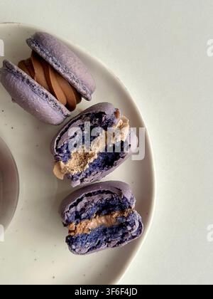 Delicious purple lavender macarons with chocolate filling, half eaten and halved on plate Stock Photo