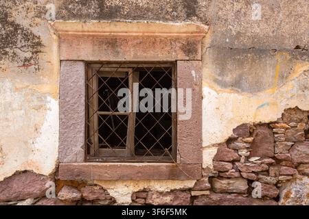 Old Broken Window with Iron Grate on Damaged Weathered Stone Wall Stock Photo