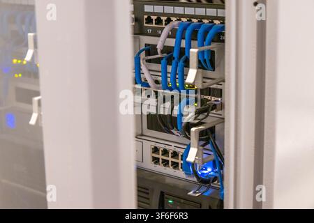 Detailed view of a server rack showing multiple network switches with organized cabling and blinking indicator lights Stock Photo