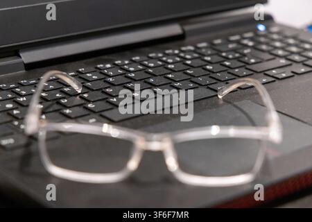 A pair of transparent reading glasses is placed on the keys of a black laptop, suggesting work or study Stock Photo