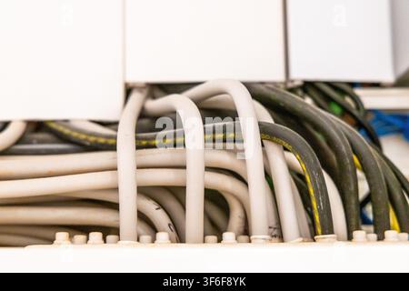A close-up view shows a neat arrangement of various electrical wires and cables, some with yellow stripes, emerging from a white housing unit Stock Photo