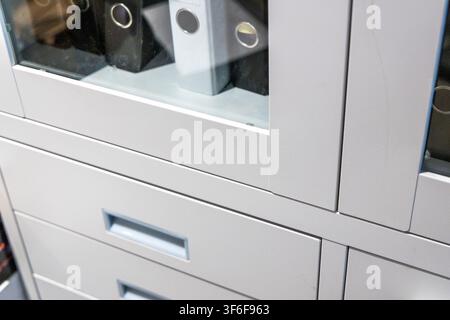 A close-up view of a sleek, contemporary office storage unit featuring transparent doors revealing binders and multiple drawers for efficient organiza Stock Photo