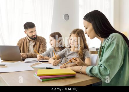 Family at home studying together, parents tutoring daughters with laptop and notes Stock Photo