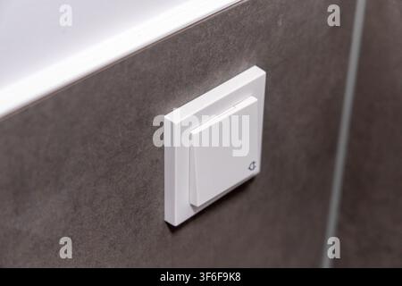 A close-up view of a contemporary white light switch mounted on a dark, textured wall, likely in a residential setting Stock Photo