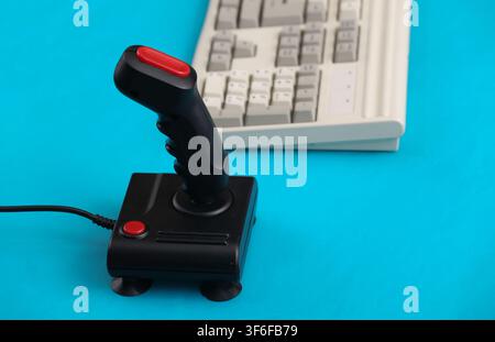 Old pc keyboard and joystick on blue background. Retro gaming. 80s. Stock Photo