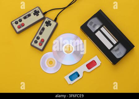 Flat lay 80s attribute composition. Gamepads, video cassette, CD's, 3D glasses. Retro Electronics, gadgets and devices. Entertainment and gaming. Yell Stock Photo
