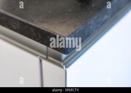 A detailed view showcases the refined edge of a dark, speckled granite countertop, highlighting its natural stone texture and smooth finish Stock Photo