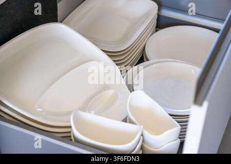 A collection of modern square and round white ceramic dishes are stored neatly in a kitchen cabinet drawer Stock Photo