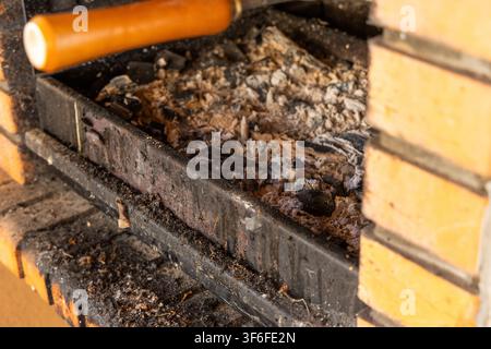 The remnants of a fire in a barbecue pit, showing burnt charcoal and ash, with a brick structure visible Stock Photo