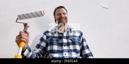 Smiling man holding paint roller ready for home painting and renovation. handyman service. copy space Stock Photo