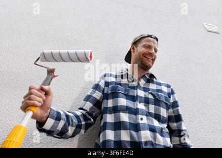 Smiling man holding paint roller ready for house painting and renovation Stock Photo